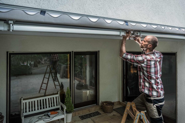 Ein Mann montiert eine Markise an einer Hauswand über einer Terrassentür.