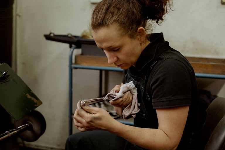 Eine Frau poliert ein Metallprodukt mit einem Tuch in einer Werkstatt.