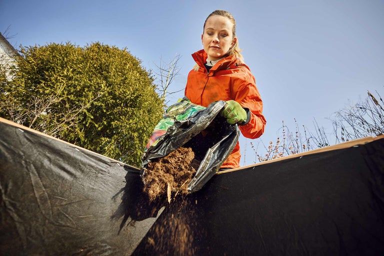 Frau schüttet Erde aus einer Tüte in ein Hochbeet