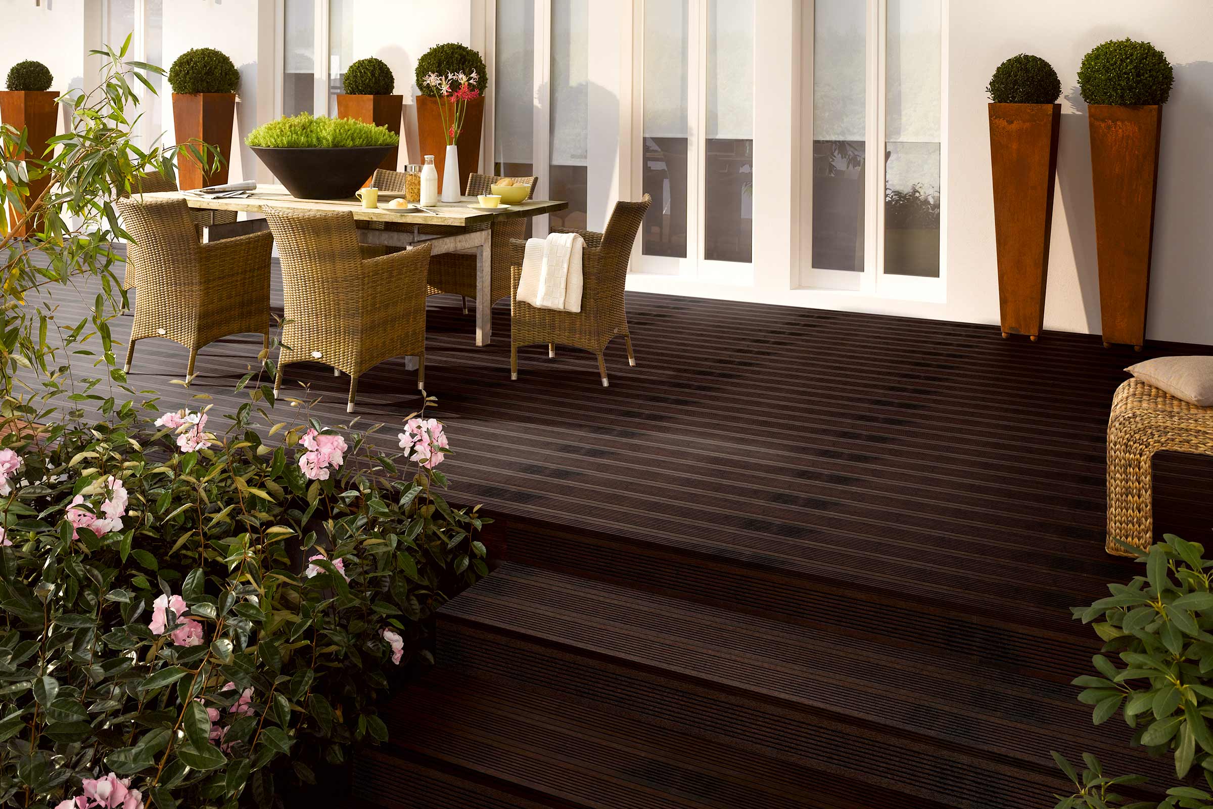 Terrasse mit dunklen Holzdielen, Gartenmöbeln und Pflanzen