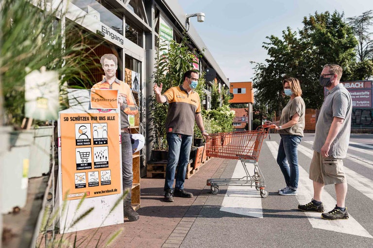 Kunden betreten den Hornbach Baumarkt, unterstützt durch Hygienemaßnahmen wie Maskenpflicht und Abstandsregeln.