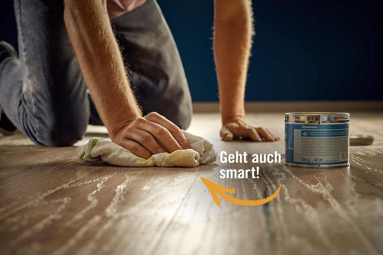 Eine Person trägt Wachs mit einem Tuch auf einen Holzboden auf.
