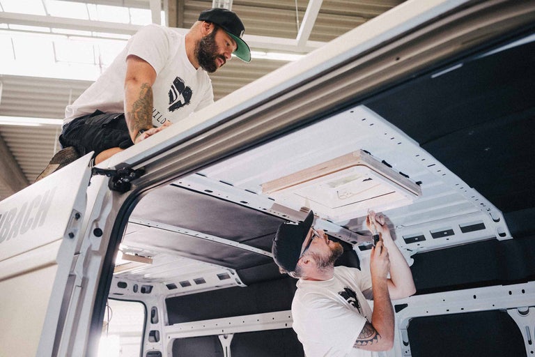 Zwei Männer montieren ein Dachfenster in einem Lieferwagen.