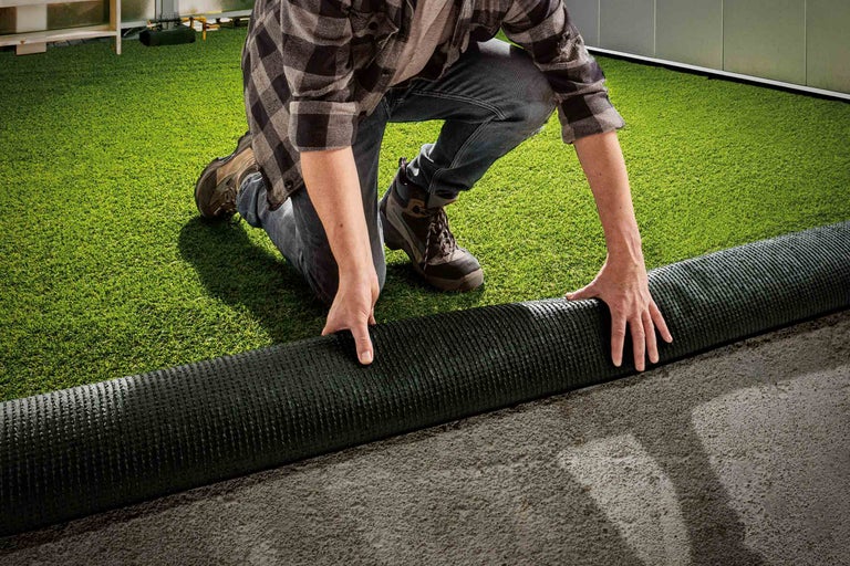 Eine Person verlegt Kunstrasen im Garten.