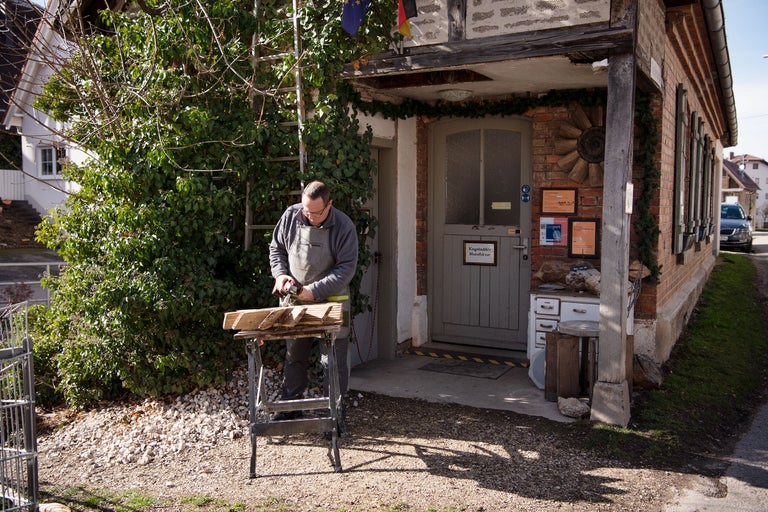 Handwerker arbeitet im Freien mit einer Säge an einem Holzbock vor einem Haus.