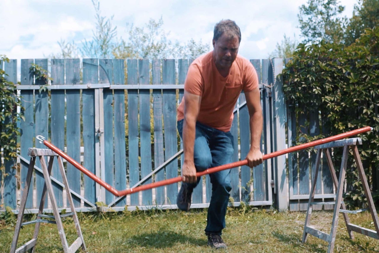 Mann biegt ein Kunststoffrohr im Garten