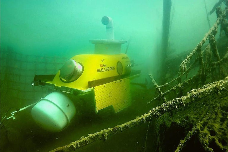 Gelbes U-Boot unter Wasser neben einem Schiffswrack