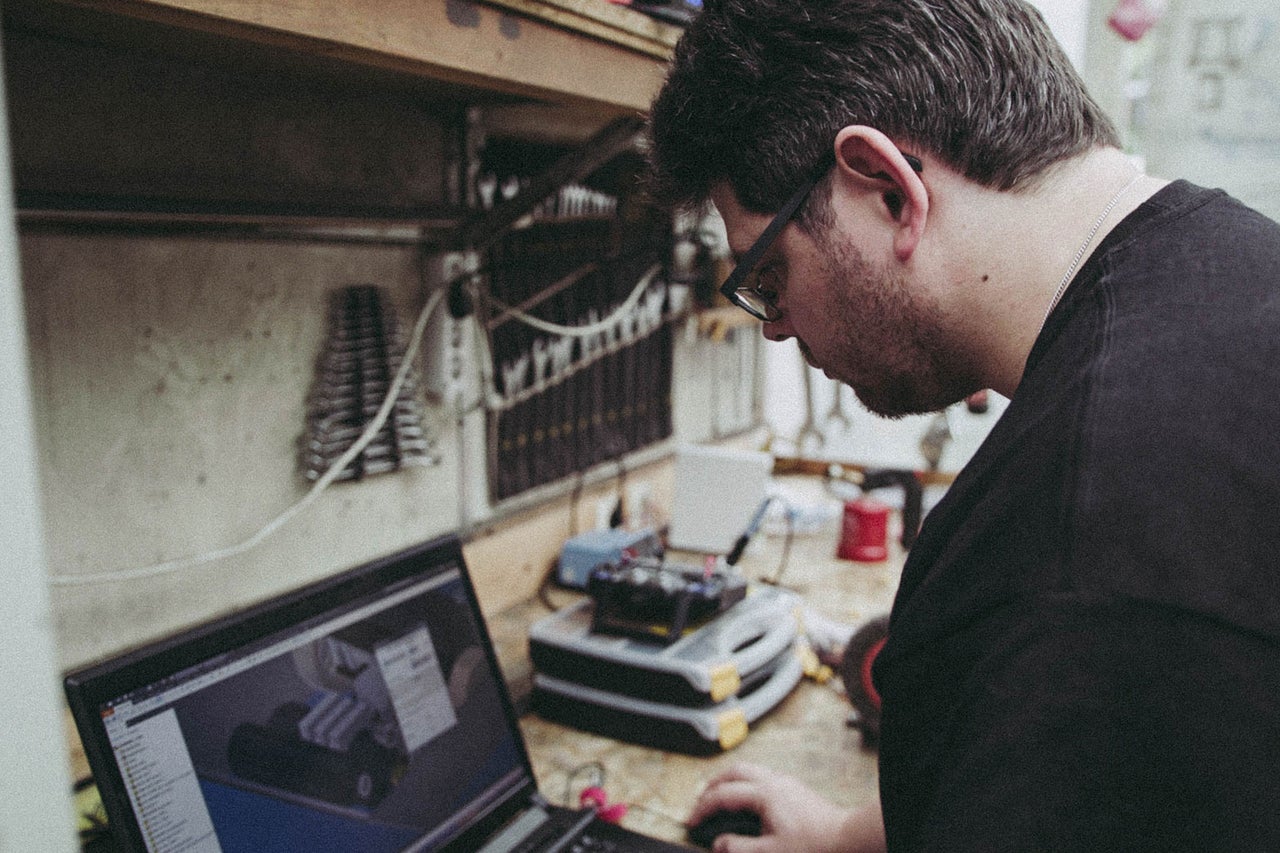 Mann mit Brille arbeitet an einem Laptop in einer Werkstatt.