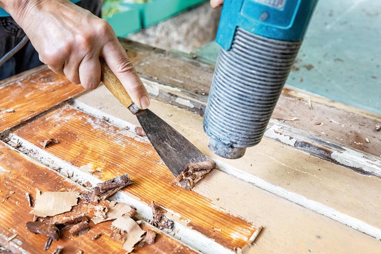 Farbe wird mit einem Heißluftgebläse und Spachtel von einer Holztür entfernt.