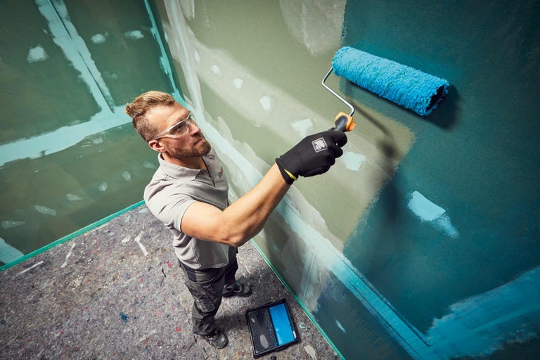 Mann streicht mit Farbroller eine Wand. Malerarbeiten in Innenräumen.
