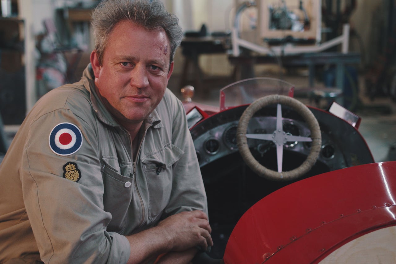 Mann in Arbeitskleidung mit Oldtimer-Rennwagen