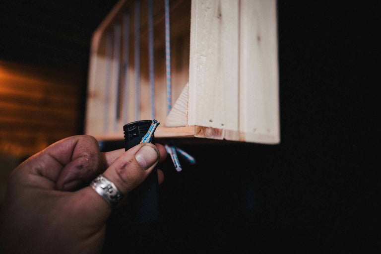 Eine Person verwendet ein Feuerzeug, um ein Seil an einem hölzernen Regal zu befestigen.