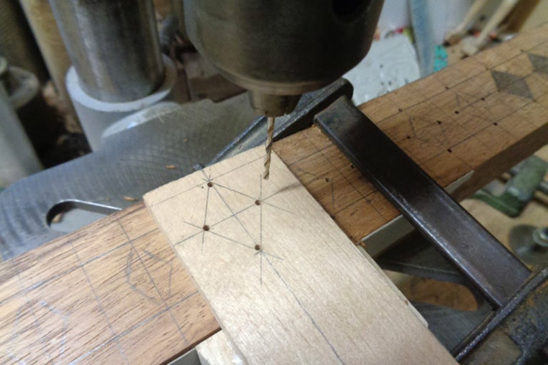 Nahaufnahme einer Bohrmaschine, die Löcher in ein Holzbrett bohrt, das mit einer Schraubzwinge befestigt ist.