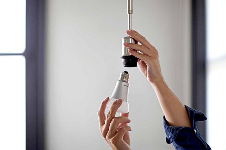 Eine Person schraubt eine Philips Glühbirne in eine Lampenfassung.