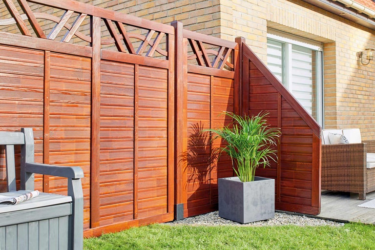 Gartenszene mit Holzzaun, Sitzbank mit Zeitungen und Topfpflanze