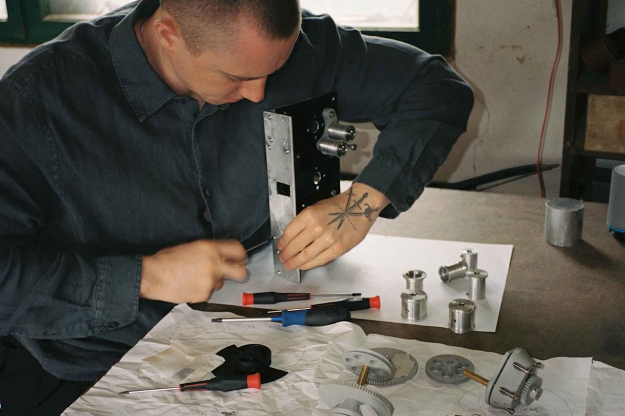 Ein Handwerker montiert an einem Werkzeugtisch mit Schraubendrehern und verschiedenen Metallbauteilen ein technisches Gerät.