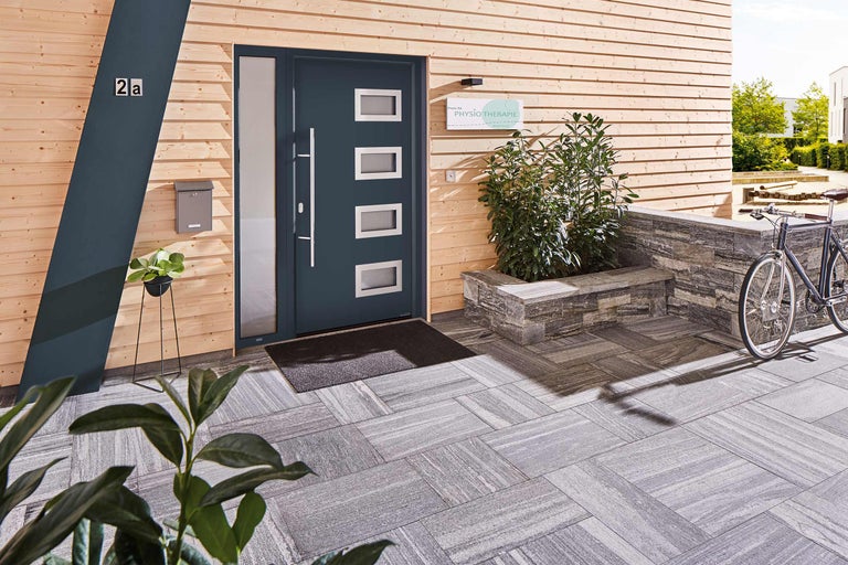 Außenansicht eines Hauses mit Holzwand, Haustür mit Fenstern, Briefkasten und Steinpflaster