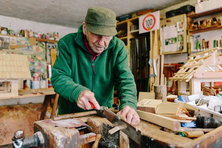 Ein Mann sägt Holz in einer Werkstatt mit Werkzeugen und Holzbauten.