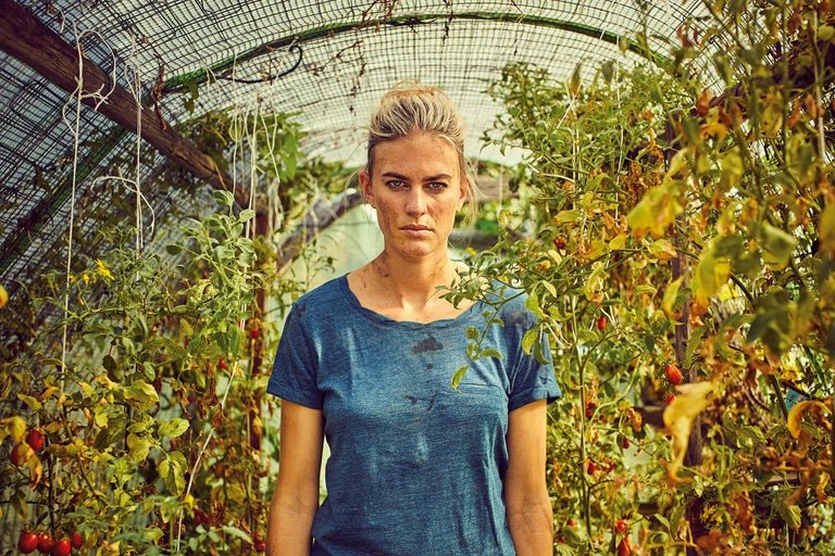 Eine Frau steht in einem Gewächshaus zwischen Tomatenpflanzen.