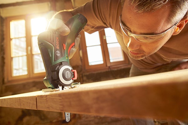 Ein Mann mit Schutzbrille bearbeitet ein Holzbrett mit einem Multifunktionswerkzeug von Bosch