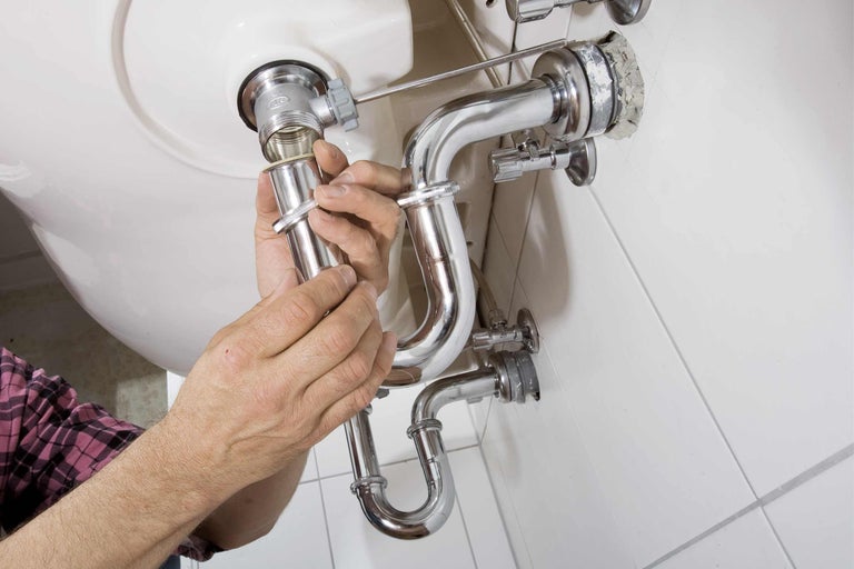 Installation eines Siphons unter einem Waschbecken mit glänzenden Rohren.