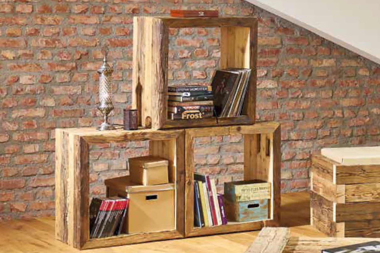 Gestapelte Regale aus Holz mit Büchern und Dekoartikeln vor einer Ziegelwand.