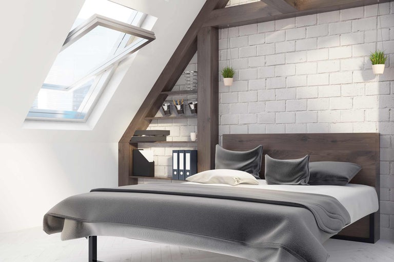 Ein Schlafzimmer im Dachgeschoss mit Dachfenster, Bett, Regal und Ziegelwand