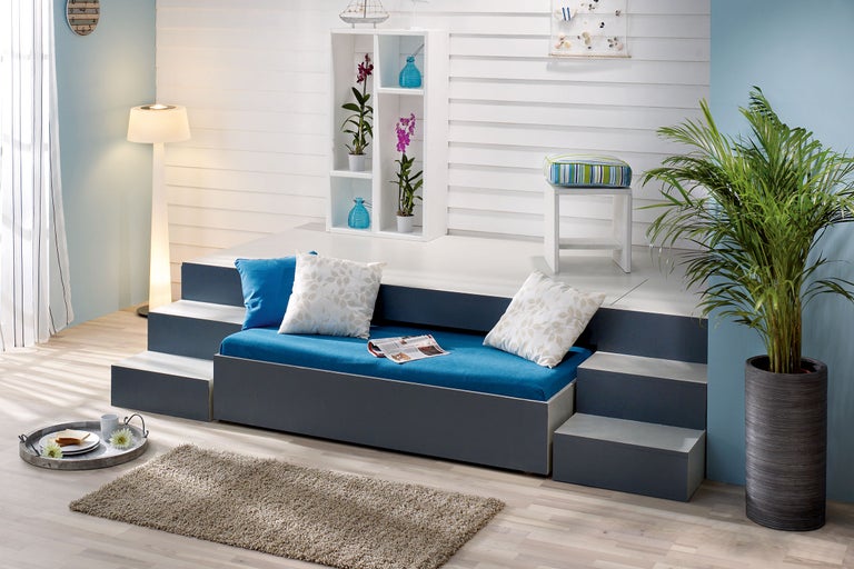 Wohnzimmer mit Stufenbett, Regal, Stehleuchte und Zimmerpflanze für eine helle und freundliche Atmosphäre