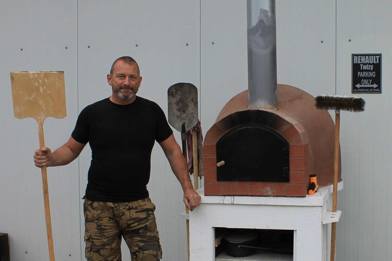 Mann mit Pizzaschieber neben Pizzaofen aus Ziegeln