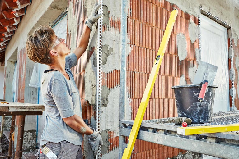 Frau montiert Putzprofile an einer Wand aus Ziegelsteinen mit Mörtel