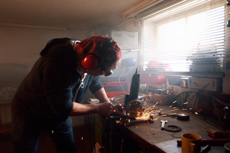 Mann arbeitet mit Winkelschleifer in Werkstatt und trägt dabei Schutzkleidung.