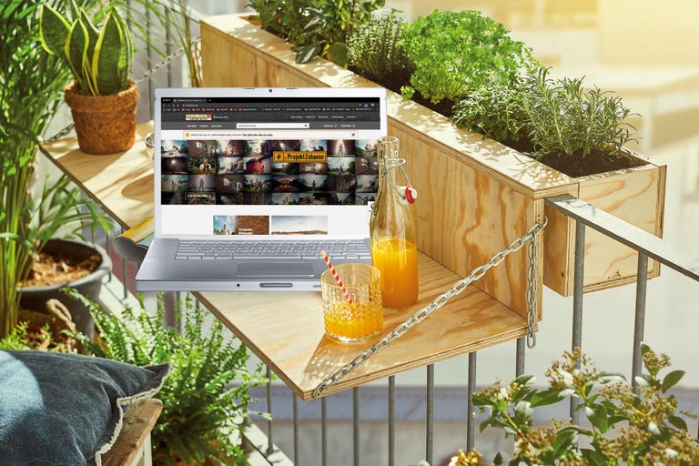 Balkonszene mit Holzkästen, Laptop und Getränken für eine entspannte Atmosphäre