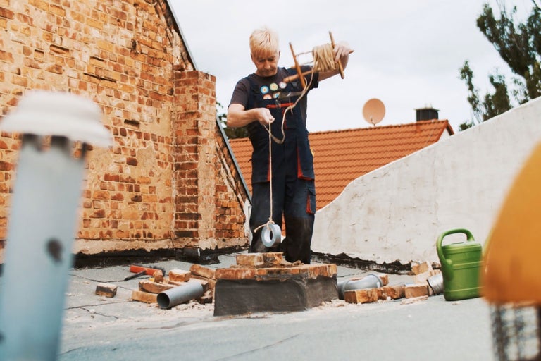 Ein Handwerker arbeitet auf einem Dach mit Ziegeln und verwendet Werkzeuge sowie eine Richtschnur mit Klebeband.