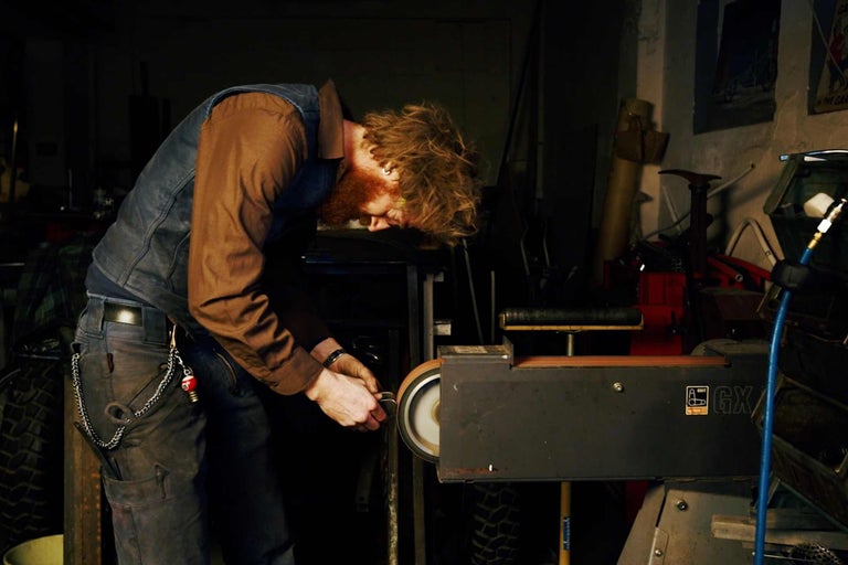 Mann arbeitet mit einem Bandschleifer in einer Werkstatt.