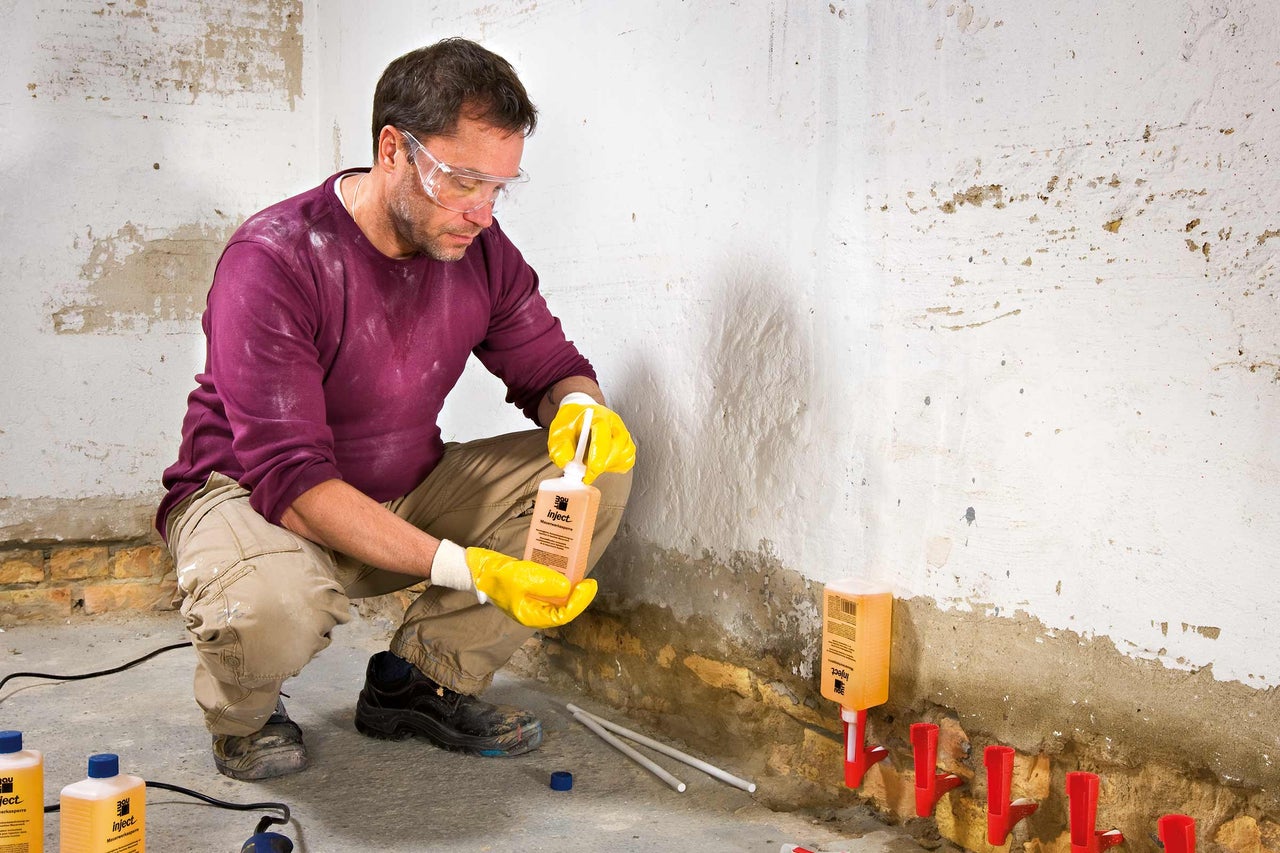 Handwerker bei der Injektion einer Horizontalsperre in eine Wand zur Mauerwerkstrockenlegung.