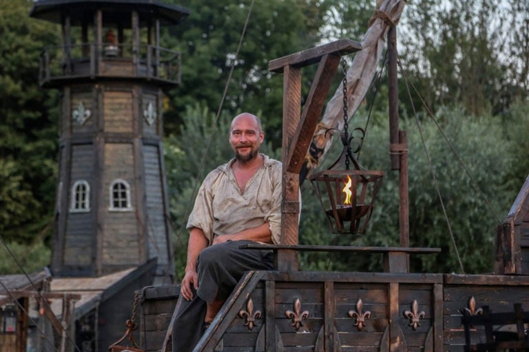 Szene mit einem Mann auf einem Holzschiff und einem Turm im Hintergrund