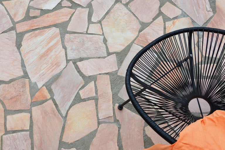 Terrasse mit Natursteinpflaster und einem Rattansessel.
