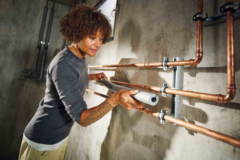 Eine Frau befestigt eine Rohrisolierung an einem Heizungsrohr.