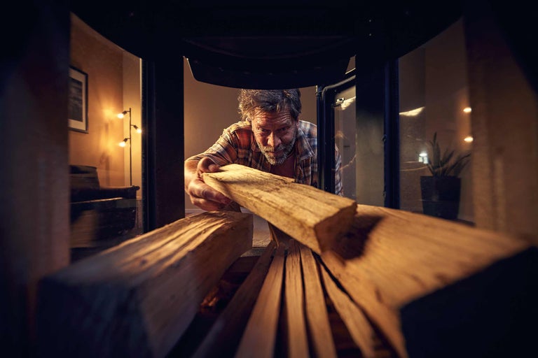 Mann legt Brennholz in einen Kaminofen