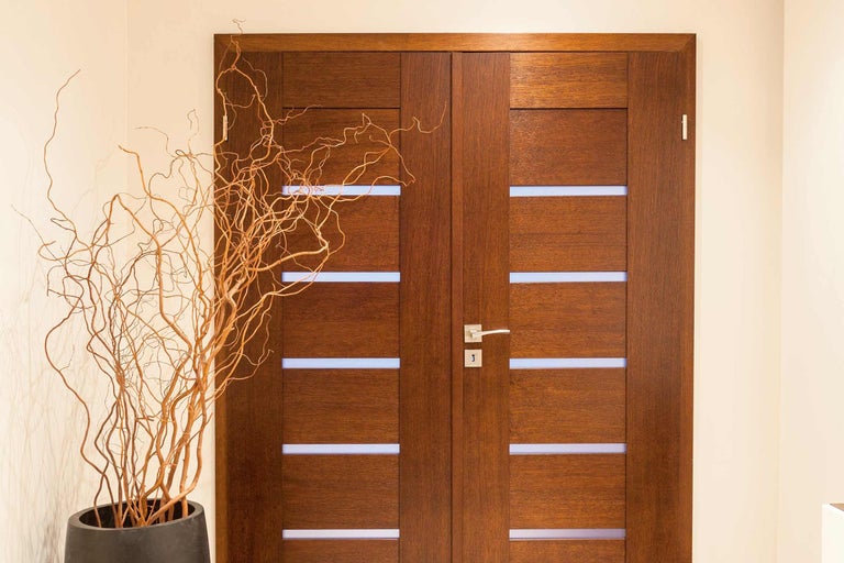 Holztür mit Glaseinsätzen und einer Dekoration aus Zweigen in einem Topf.