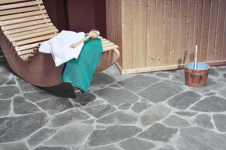 Sauna-Interieur mit Liege, Handtüchern, Aufgusskübel und Steinboden