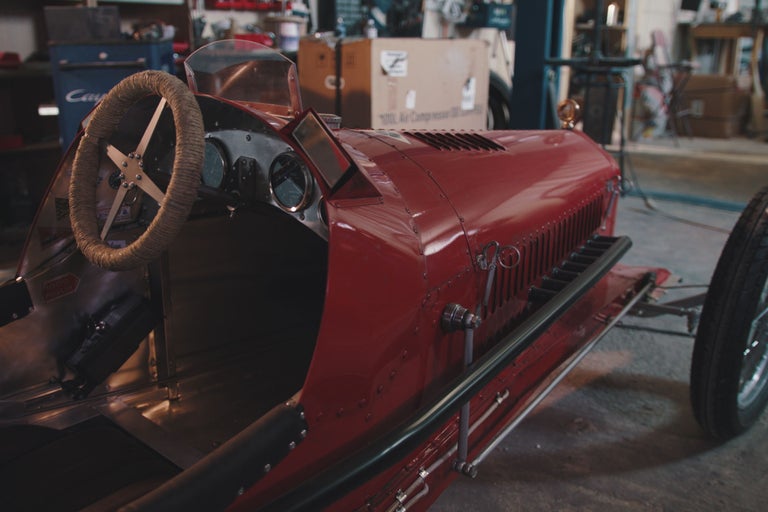 Detailansicht eines roten Oldtimer-Rennwagens mit Lenkrad, Armaturenbrett und Kühlergrill