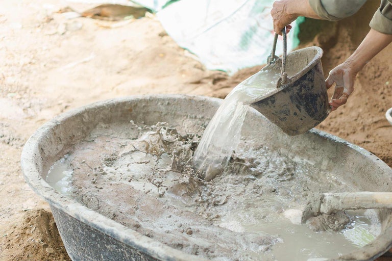 Anmischen von Beton in einer Mörtelwanne mit einem Eimer Wasser.