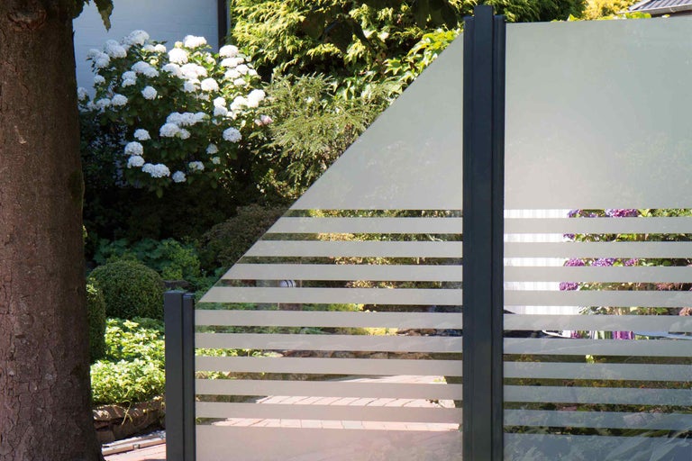 Dekorative Gartenzaunelemente mit horizontalen Streifen und Pflanzen im Hintergrund.