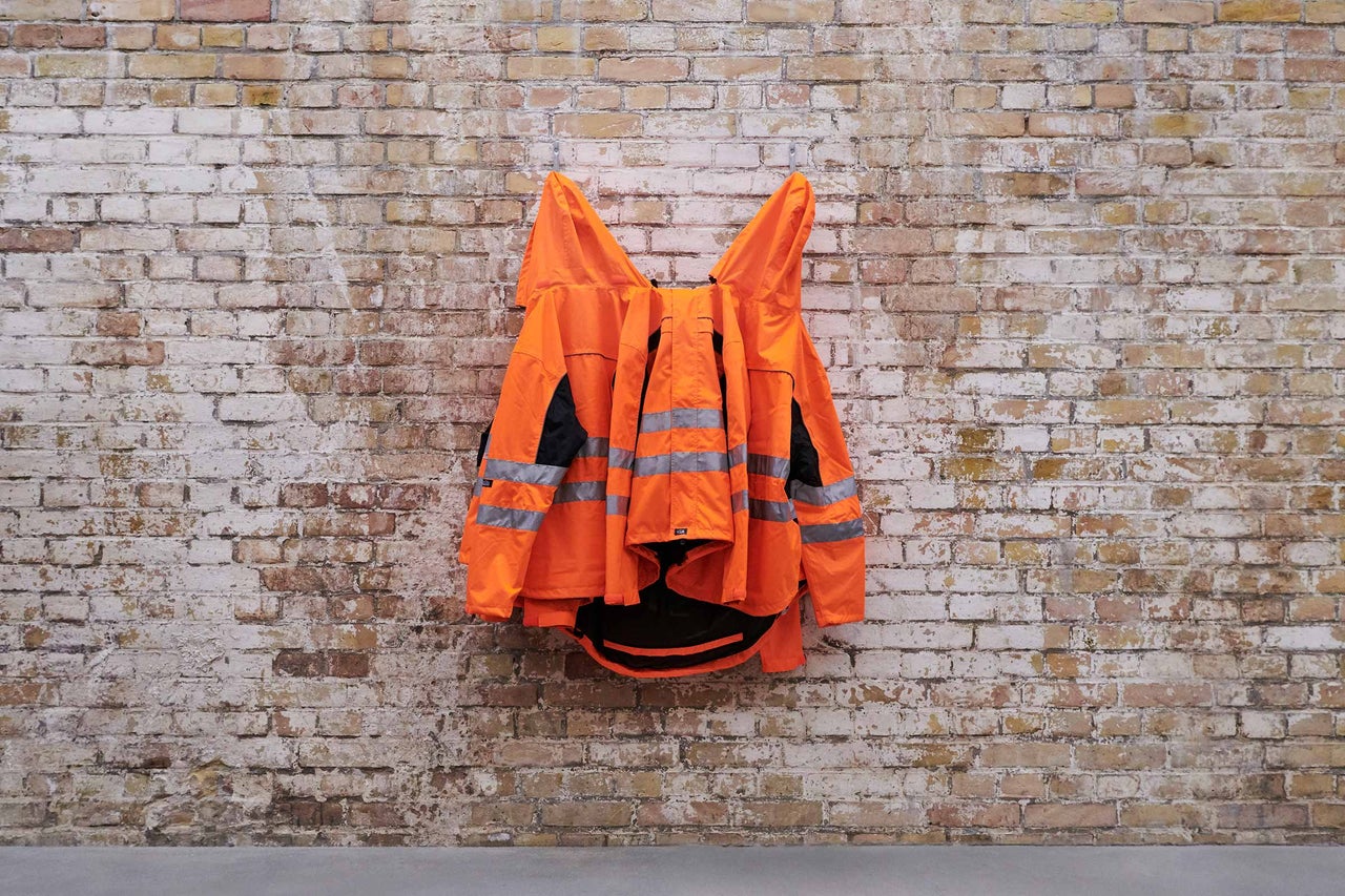 Orangefarbene Warnjacke mit Reflektorstreifen an einer Ziegelwand