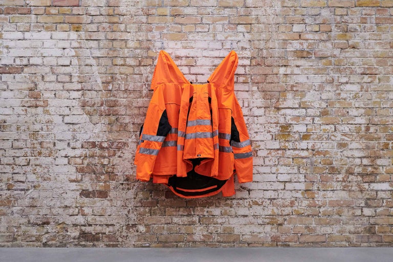 Orangefarbene Warnjacke mit Reflektorstreifen an einer Ziegelwand