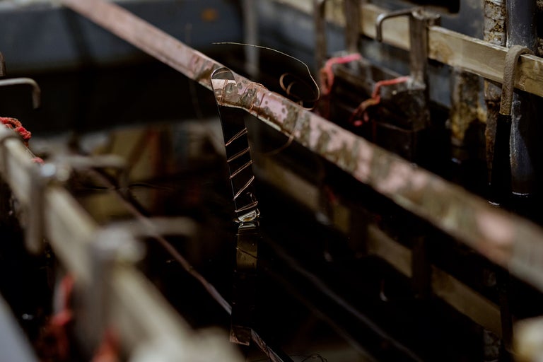 Metallteil hängt an einer Metallschiene in einer Flüssigkeit