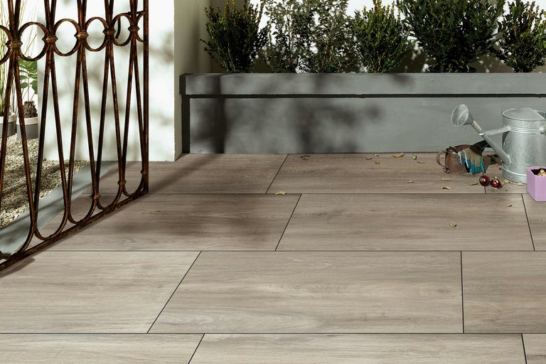 Terrasse mit Holzbodenfliesen, Eisenzaun und Bepflanzung