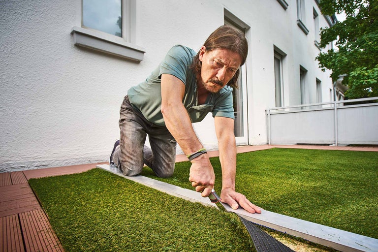 Mann verlegt Kunstrasen auf einem Balkon