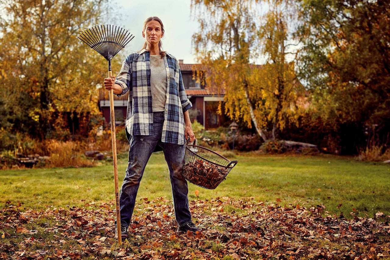 Frau mit Laubbesen und Laubkorb im Garten